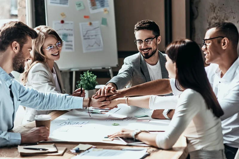 Team members joining hands over a table